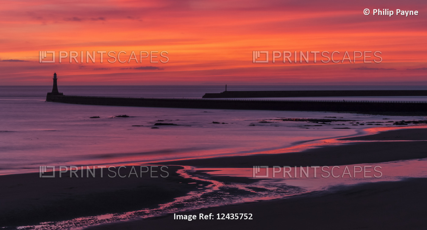 Silhouette of a pier and lighthouse with dramatic and vibrant sunrise colours ...