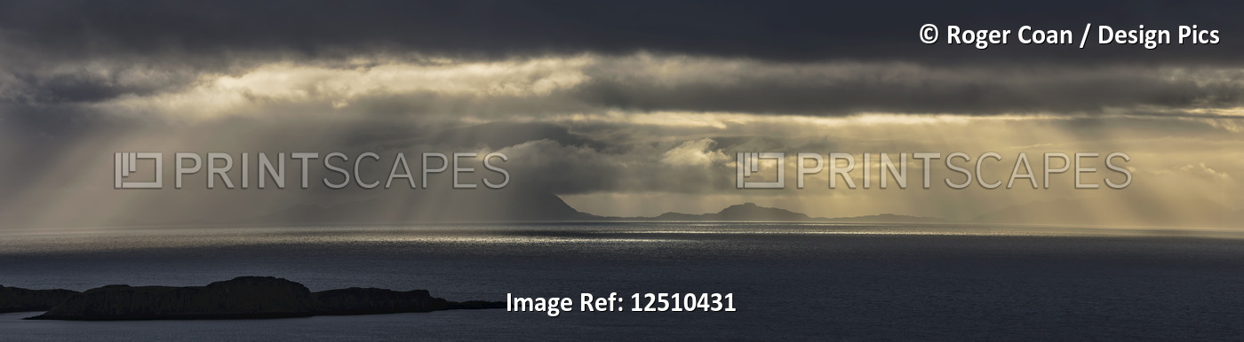Crepuscular rays shining through the storm clouds onto the ocean water; Isle of ...